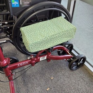 May include: A red, three-wheeled walker with a green and white patterned seat cushion. The walker has a black frame and black wheels. The walker is labeled "Dalton Care with Aluminum".