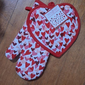 May include: A white oven mitt and pot holder set with a red heart pattern. The pot holder is heart-shaped with a red border. The oven mitt has a red trim. A tag reads "RICH HOME Oven mitt & Pot Holder."
