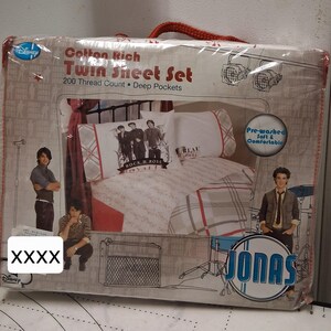 May include: A packaged Twin Sheet Set with a Disney logo. The packaging features images of a band, with the text "Cotton Rich Twin Sheet Set" and "200 Thread Count Deep Pockets". The sheet set includes a pillowcase with the band's image.
