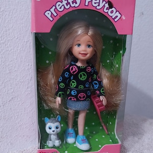 May include: A pink and green box with a doll and a puppy inside. The doll has blonde hair, a blue and black shirt with peace signs, blue jeans, and blue sneakers. The puppy is gray and white with blue eyes. The box says "Pretty Peyton" and "Li'l ones" on it. The box also has a warning label that says "CHOKING HAZARD - Small parts. Not for children under 3 years."