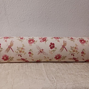 May include: A white fabric cylinder with a floral pattern featuring red flowers and dragonflies. The fabric has a subtle texture.
