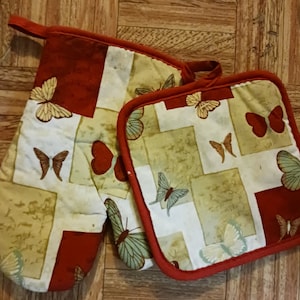 May include: A set of two red and white oven mitts with a butterfly pattern. The larger mitt is a potholder with a loop for hanging. The smaller mitt is a hot pad.