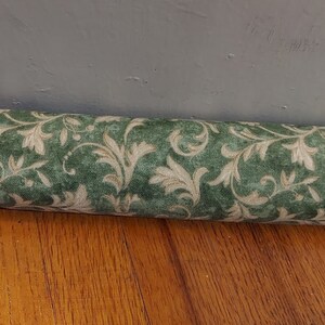 May include: A green and cream patterned doorstop with a floral design. The doorstop is made of fabric and is rolled up.