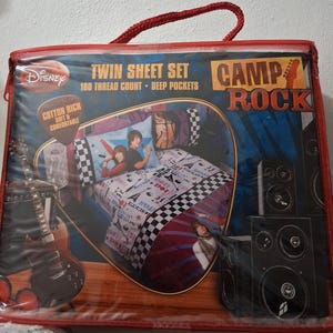 May include: A red-trimmed package containing a Disney Camp Rock twin sheet set. The set includes a pillowcase and sheets with a musical theme, featuring images of the movie's characters. The package also displays text that reads "180 thread count" and "deep pockets."