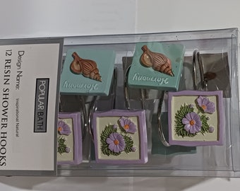 May include: A set of 12 resin shower hooks in a clear plastic package. The hooks feature square designs with seashell and flower motifs in pastel colors. The word "Harmony" is on the seashell hooks. The package is labeled "Popular Bath".