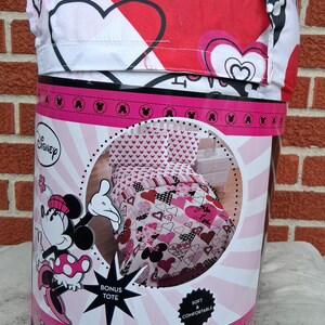 May include: A Disney Minnie Mouse microfibre full comforter set in packaging. The bedding features a red, pink, white, and black heart pattern with Minnie Mouse graphics. The packaging includes a bonus tote and measures 193 cm by 218 cm.