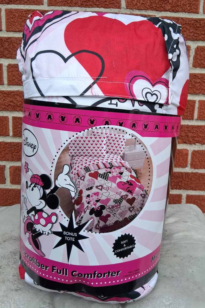 May include: A Disney Minnie Mouse microfibre full comforter set in packaging. The bedding features a red, pink, white, and black heart pattern with Minnie Mouse graphics. The packaging includes a bonus tote and measures 193 cm by 218 cm.