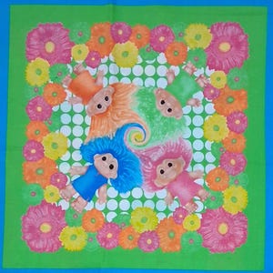 May include: A green textile featuring a whimsical design of troll dolls with colorful hair, surrounded by a border of flowers in pink, orange, and yellow. The dolls are arranged around a white polka-dot pattern.