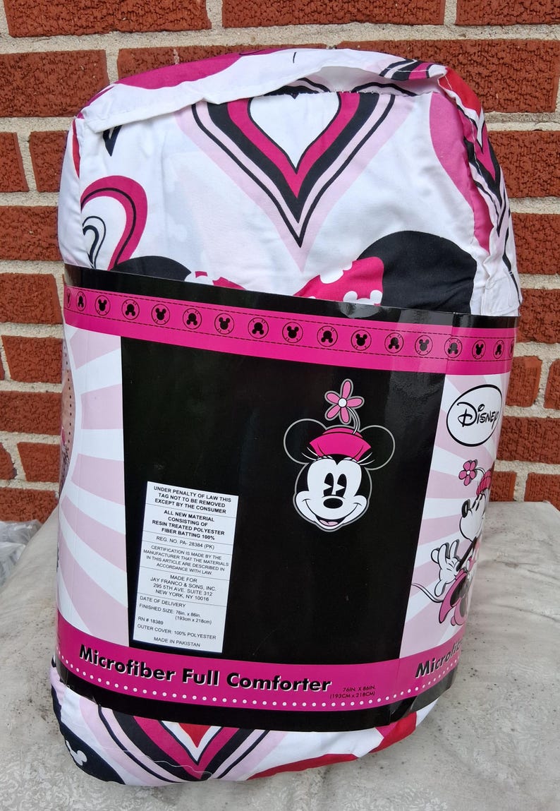 May include: A Disney Minnie Mouse microfibre full comforter packaged in plastic. The comforter features a white, pink, and black heart pattern. The packaging label displays the Disney logo, a Minnie Mouse graphic, and text stating 193cm x 218cm.