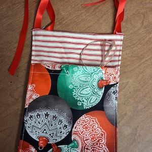 May include: A fabric Christmas ornament bag with red ribbon ties. The bag features a pattern of colorful ornaments on a black background. The top of the bag has a red and white striped pattern.
