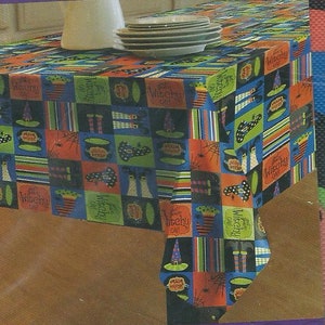 May include: A colorful Halloween tablecloth with a patchwork design featuring witches, hats, and the text "Witchy Oh!" in a black, orange, green, and blue color scheme.