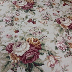 May include: Cream-colored fabric with a repeating floral pattern. The design features large roses in shades of white, pink, and burgundy, interspersed with smaller flowers and green foliage. Small red berries add a touch of detail to the overall design.