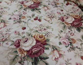 May include: Cream-colored fabric with a repeating floral pattern. The design features large roses in shades of white, pink, and burgundy, interspersed with smaller flowers and green foliage. Small red berries add a touch of detail to the overall design.