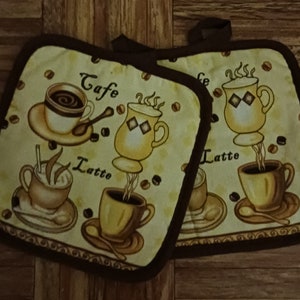 May include: Two yellow and brown pot holders with a coffee theme. The pot holders feature illustrations of coffee cups and the words "Cafe", "Latte", and "Cappuccino".