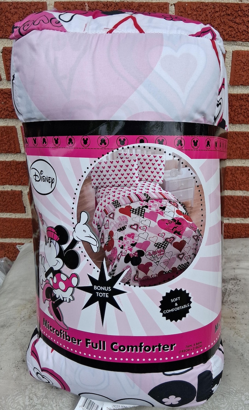 May include: A Disney Minnie Mouse microfibre full comforter set in packaging. The bedding features a pink, white, and black heart and character pattern. The packaging indicates a 193 cm by 218 cm size, includes a bonus tote, and is labelled as soft and comfortable.