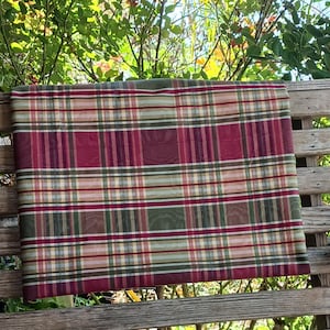 May include: Red, green, and cream plaid tablecloth hanging on a wooden porch swing.