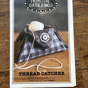 May include: A printed card featuring a gray and white plaid thread catcher with a white ball of yarn inside. The text "THREAD CATCHER" is displayed below the image. Approximate size is 2" x 4".