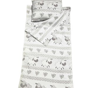 Può includere: Un set di biancheria da letto bianco con un motivo ripetuto di pecore e piccoli uccelli grigi, separati da fasce orizzontali a pois grigi e bianchi. Il set include un cuscino rettangolare e una coperta abbinata con un angolo ripiegato.