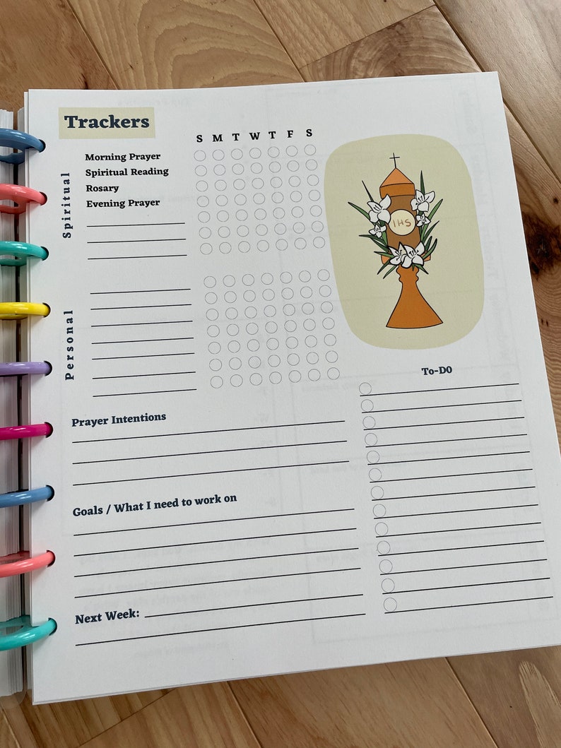 May include: A printable planner page with a daily tracker for spiritual and personal goals. The page includes sections for morning prayer, spiritual reading, rosary, evening prayer, prayer intentions, goals, and to-do list. The page also features a graphic of a religious symbol with the letters IHS.