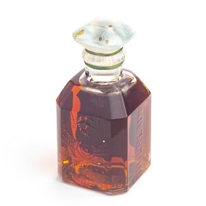 May include: A vintage perfume bottle with a geometric design. The bottle is filled with a dark amber liquid and has a light blue and white stopper. The word "GUERLAIN" is printed vertically on the side of the bottle.