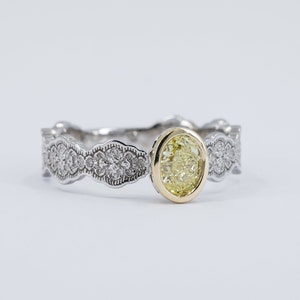 May include: A silver ring with a yellow oval-shaped gemstone set in a gold bezel. The band is decorated with a delicate, intricate design of small diamonds.