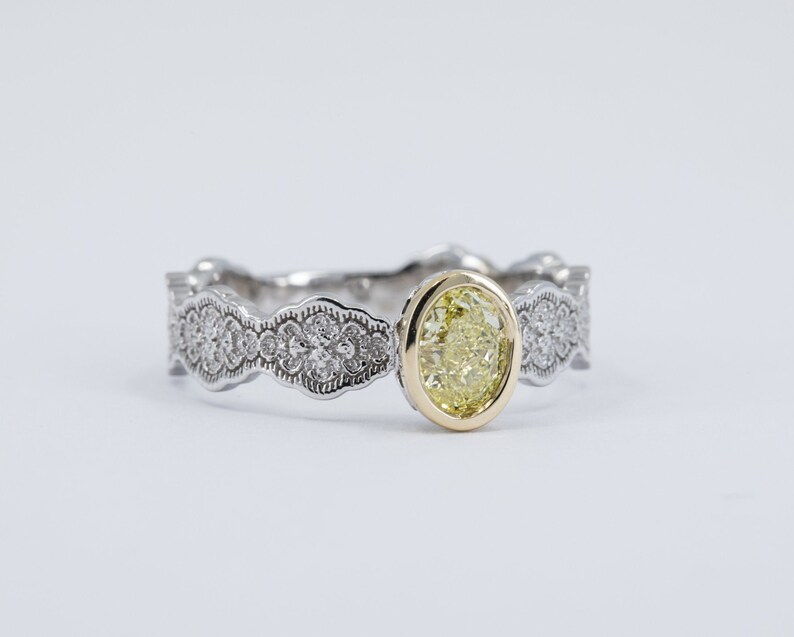 May include: A silver ring with a yellow oval-shaped gemstone set in a gold bezel. The band is decorated with a delicate, intricate design of small diamonds.