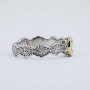 May include: A delicate, white gold engagement ring with a yellow gold band and a round, bezel-set diamond. The band is adorned with a scalloped design and small diamonds.