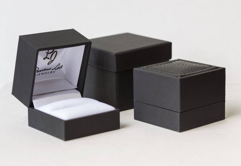 May include: Three black ring boxes. The largest box has a white interior and the text "Precious Lace Jewelry" printed on the inside of the lid.