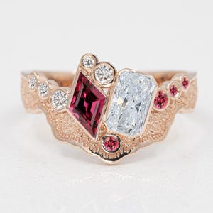 May include: A rose gold ring with a large, rectangular diamond and a smaller, square ruby. The ring is set with smaller diamonds and rubies around the main stones. The band is intricately detailed with a floral design.