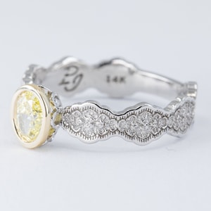 May include: A 14k white gold engagement ring with a yellow oval diamond set in a yellow gold bezel. The band is decorated with a scalloped design and pave set diamonds.