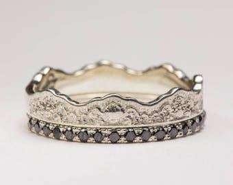 May include: A silver ring with a textured, wavy band and a row of black diamonds.