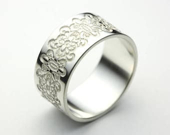 Puede incluir: Un anillo de plata con un diseño floral decorativo alrededor de la banda.