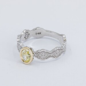 May include: A yellow gold and white gold ring with a yellow oval gemstone set in the center. The band is decorated with a scalloped design and small diamonds.