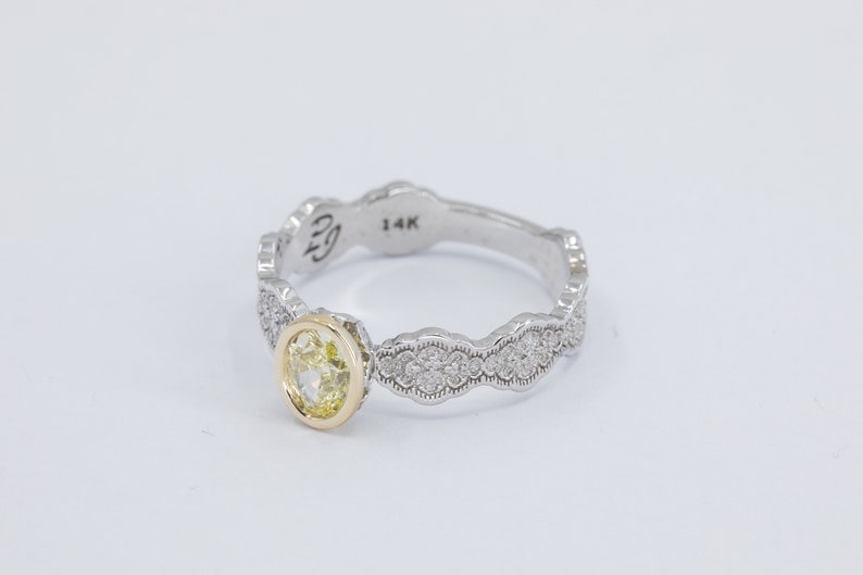 May include: A yellow gold and white gold ring with a yellow oval gemstone set in the center. The band is decorated with a scalloped design and small diamonds.