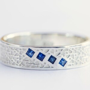 May include: A silver band ring with a textured surface and four small blue square gemstones.