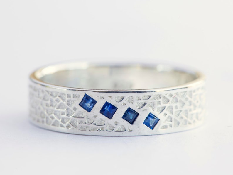 May include: A silver band ring with a textured surface and four small blue square gemstones.