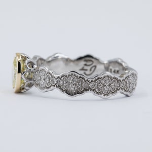 May include: A yellow gold and white gold engagement ring with a pear-shaped diamond set in a delicate, ornate setting. The band is adorned with a row of smaller diamonds.