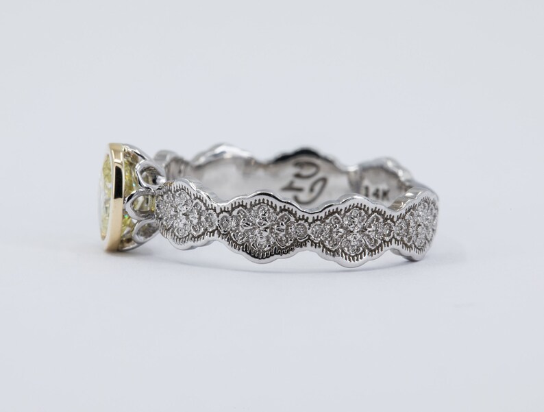 May include: A yellow gold and white gold engagement ring with a pear-shaped diamond set in a delicate, ornate setting. The band is adorned with a row of smaller diamonds.