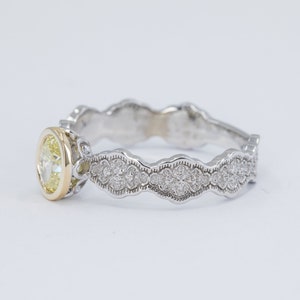 May include: A delicate, white gold engagement ring with a yellow diamond center stone and a scalloped band adorned with smaller diamonds.