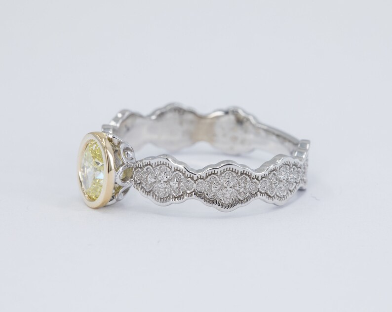 May include: A delicate, white gold engagement ring with a yellow diamond center stone and a scalloped band adorned with smaller diamonds.