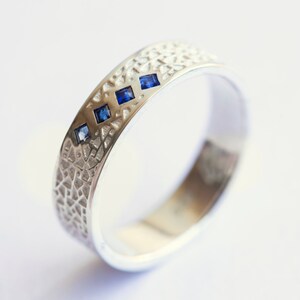 May include: A silver band ring with a textured surface and three small blue gemstones.