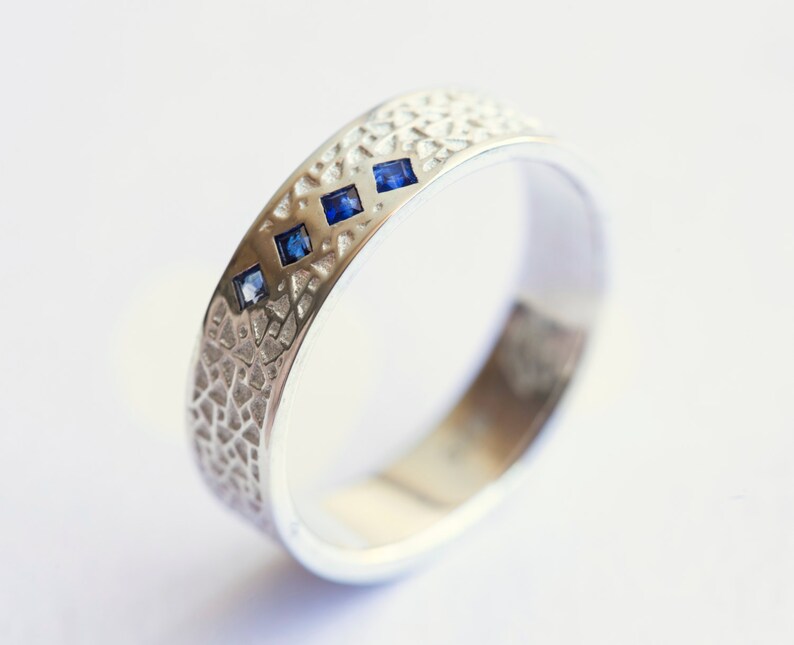 May include: A silver band ring with a textured surface and three small blue gemstones.