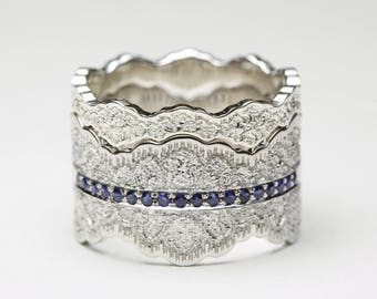 Op de afbeelding: Een stapelbare zilveren ring met een getextureerd oppervlak en een rij kleine blauwe edelstenen. De ring heeft een geschulpte rand en staat tegen een witte achtergrond.