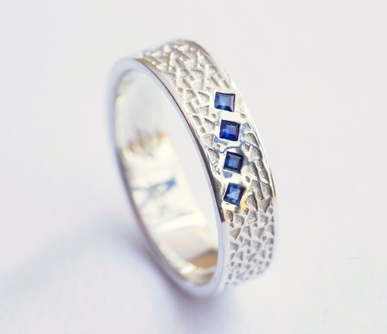 May include: A silver band ring with a textured surface and four small blue gemstones.