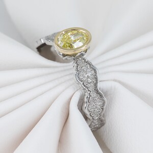 May include: A silver ring with a yellow oval-shaped gemstone set in a gold bezel. The band is decorated with small diamonds.