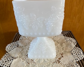 May include: White milk glass pedestal bowl with a grapevine design. The bowl is square and has a raised base.