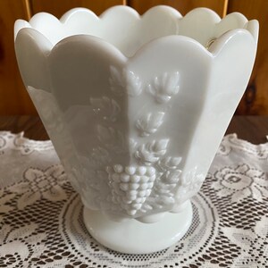 May include: White milk glass vase with a scalloped rim and embossed grape design.