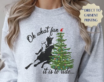May include: Gray sweatshirt with a Christmas tree and a silhouette of a person riding a horse. The text on the sweatshirt reads "Oh what fun it is to ride..."