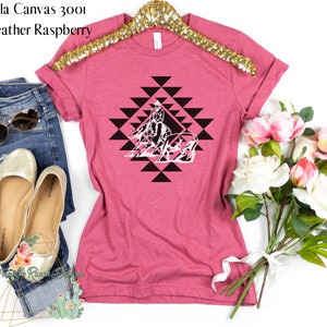 May include: A pink Bella Canvas 3001 t-shirt with a black and white graphic of a horse and rider in a geometric pattern. The shirt is heather raspberry.