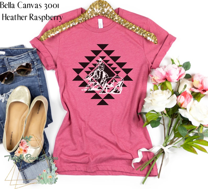 May include: A pink Bella Canvas 3001 t-shirt with a black and white graphic of a horse and rider in a geometric pattern. The shirt is heather raspberry.